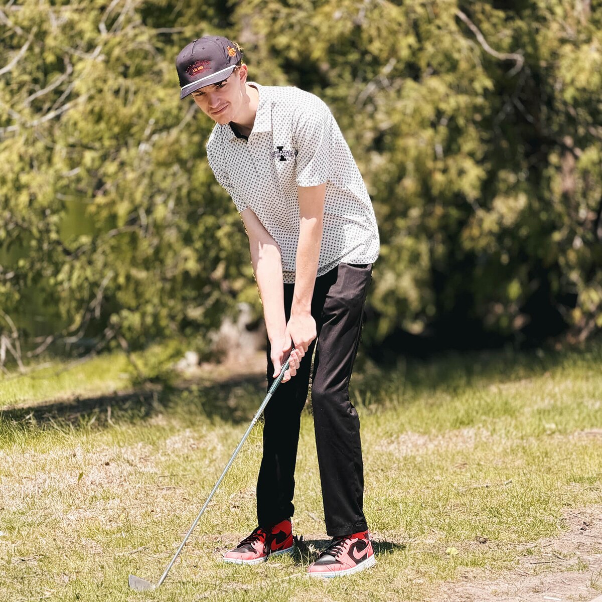 Student swinging a golf club wearing Swannies I-State Black and White Pattern Hazelwood Polo